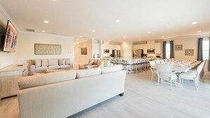 Een ruime woonkamer met een grote bank, een eettafel gedekt voor zes personen, en een keuken op de achtergrond.
