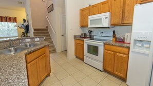 A kitchen with granite countertops, wooden cabinets, a microwave, stove, and a refrigerator. - Rent a Luxury Villa on Encantada Resort, Minutes From Disney, Orlando Villa 1062 (Kissimmee)