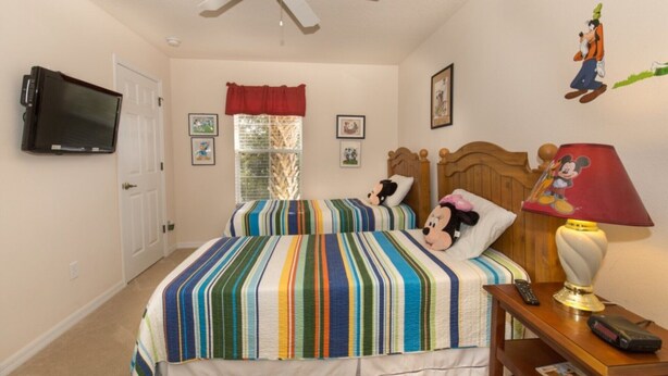 A bedroom with a bed, a ceiling fan, a television, a window with curtains, and a Mickey Mouse lamp. - Rent a Luxury Villa on Encantada Resort, Minutes From Disney, Orlando Villa 1062 (Kissimmee)