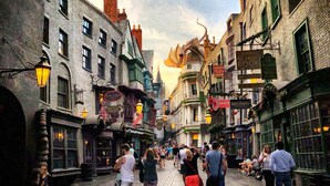 Une rue animée, bordée de bâtiments historiques, avec une statue de dragon et une foule de personnes.