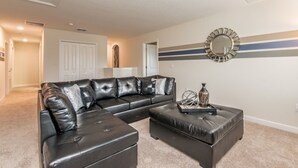 A living room with a black leather sectional sofa, a matching ottoman, and a decorative mirror on the wall. - Rent a Luxury Villa on Champions Gate Resort, Minutes From Disney, Orlando Villa 1437 (Davenport)
