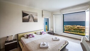 Un dormitorio con cama, mesita de noche, ventana con vista al mar y un cuadro en la pared.