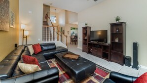 Un salon avec un canapé en cuir noir, un téléviseur à écran plat et un meuble de rangement en bois.