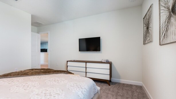 A bedroom with a bed, a dresser, a television, and artwork on the walls. - The Ultimate Guide to Renting Your Luxury 8 Bedroom Mansion on Champions Gate Resort, Orlando Mansion 2526 (Davenport)