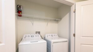 A laundry room with two stacked front-loading washing machines and a fire extinguisher on a shelf. - The Ultimate Guide to Renting Your Luxury 8 Bedroom Mansion on Champions Gate Resort, Orlando Mansion 2526 (Davenport)