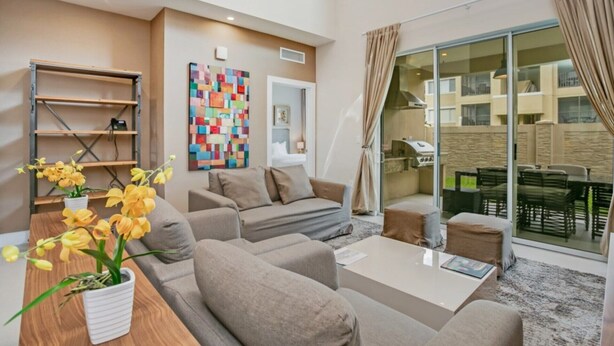 Ein modernes Wohnzimmer mit einer Couch, einem Couchtisch und einer Zimmerpflanze. An der Wand hängt ein farbenfrohes Kunstwerk, und ein Balkon ist mit Gartenmöbeln ausgestattet.