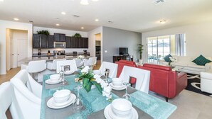 Un salón amplio con una mesa de comedor dispuesta para seis personas, un sofá rojo y un televisor al fondo.