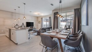 A modern kitchen with a central island, dining area with a long table and chairs, and a living area with a sofa and TV. - Rent a Luxury Townhome on Storey Lake Resort, Minutes From Disney, Orlando Townhome 3093 (Kissimmee)
