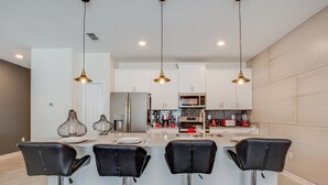 A modern kitchen with a central island, bar stools, stainless steel appliances, and pendant lighting. - Rent a Luxury Townhome on Storey Lake Resort, Minutes From Disney, Orlando Townhome 3093 (Kissimmee)