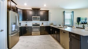 A modern kitchen with dark cabinetry, stainless steel appliances, and a marble floor. - Picture Renting Your Own Luxury Mansion on the Exclusive Champions Gate Resort, Close to Disney, Orlando Mansion 2599 (Davenport)