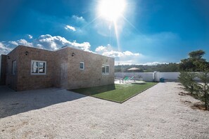 A modern building with a stone facade, a small patio area with artificial grass, and a clear sky. - Rent a Luxury Villa in Cyprus Close to the Beach, Protaras Villa 1194 (Paralimni)