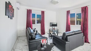 A modern living room with black leather sofas, a flat-screen TV, and a small table with two glasses. - Rent a Luxury Villa in Cyprus Close to the Beach, Protaras Villa 1194 (Paralimni)