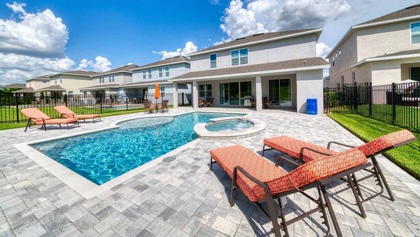 A swimming pool with lounge chairs and a hot tub, surrounded by a patio area with a covered seating area and a fenced yard. - Rent the Perfect 8 Bedroom Villa on Encore Resort at Reunion, Orlando Villa 4474 (Kissimmee)