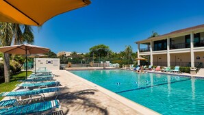 A swimming pool with lounge chairs and umbrellas, surrounded by a building with multiple balconies.