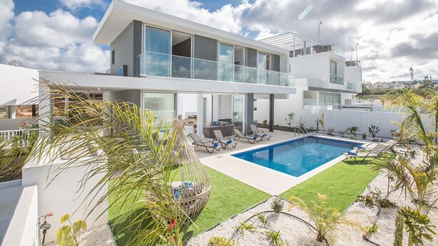 Ein modernes, zweistöckiges Haus mit großem Glasbalkon, Schwimmbecken und gepflegtem Rasen.