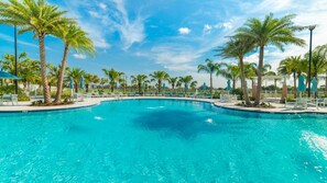 Une piscine d’un bleu éclatant, entourée de palmiers et de chaises longues.