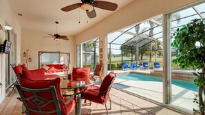 Um pátio interno amplo com piscina envidraçada, móveis vermelhos e ventiladores de teto.