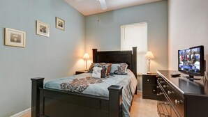 Um quarto com cama, mesas de cabeceira, televisão e quadros nas paredes.