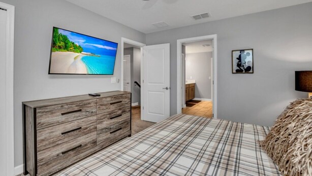 Ein Schlafzimmer mit Bett, Kommode, Deckenventilator, Fernseher und einer Tür zu einem anderen Raum.
