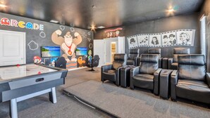 Ein Zimmer mit Billardtisch, Gaming-Stühlen und einer Wand, die mit Postern von Videospielen und Filmen dekoriert ist.