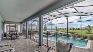 Ein überdachter Patio-Bereich mit Pool, Sitzgelegenheiten im Freien und Blick auf eine Wiese.