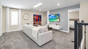 A modern living room with a white sofa, a flat-screen TV mounted on the wall, and a large window with blinds. - Picture Renting Your Own Luxury Mansion on the Exclusive Storey Lake Resort, Close to Disney, Orlando Mansion 5043 (Kissimmee)