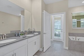 Une salle de bain moderne avec deux lavabos, un grand miroir et une porte donnant sur une autre pièce.