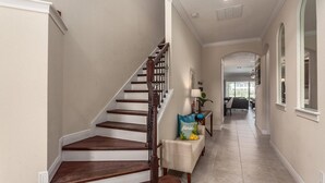 A staircase with wooden steps and a dark handrail, leading to a hallway with a light-colored floor and a view of a dining area in the background. - Luxury Private Villa With Large Pool on Reunion Resort and Spa, Orlando Villa 4588 (Kissimmee)