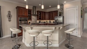 A modern kitchen with a central island, bar stools, stainless steel appliances, and pendant lighting. - Luxury Private Villa With Large Pool on Reunion Resort and Spa, Orlando Villa 4588 (Kissimmee)