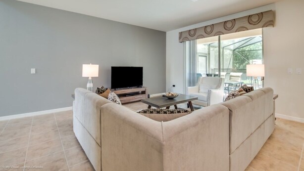 Una sala de estar con un sofá color beige, una mesa de centro, un televisor de pantalla plana y un ventanal con vistas al exterior.
