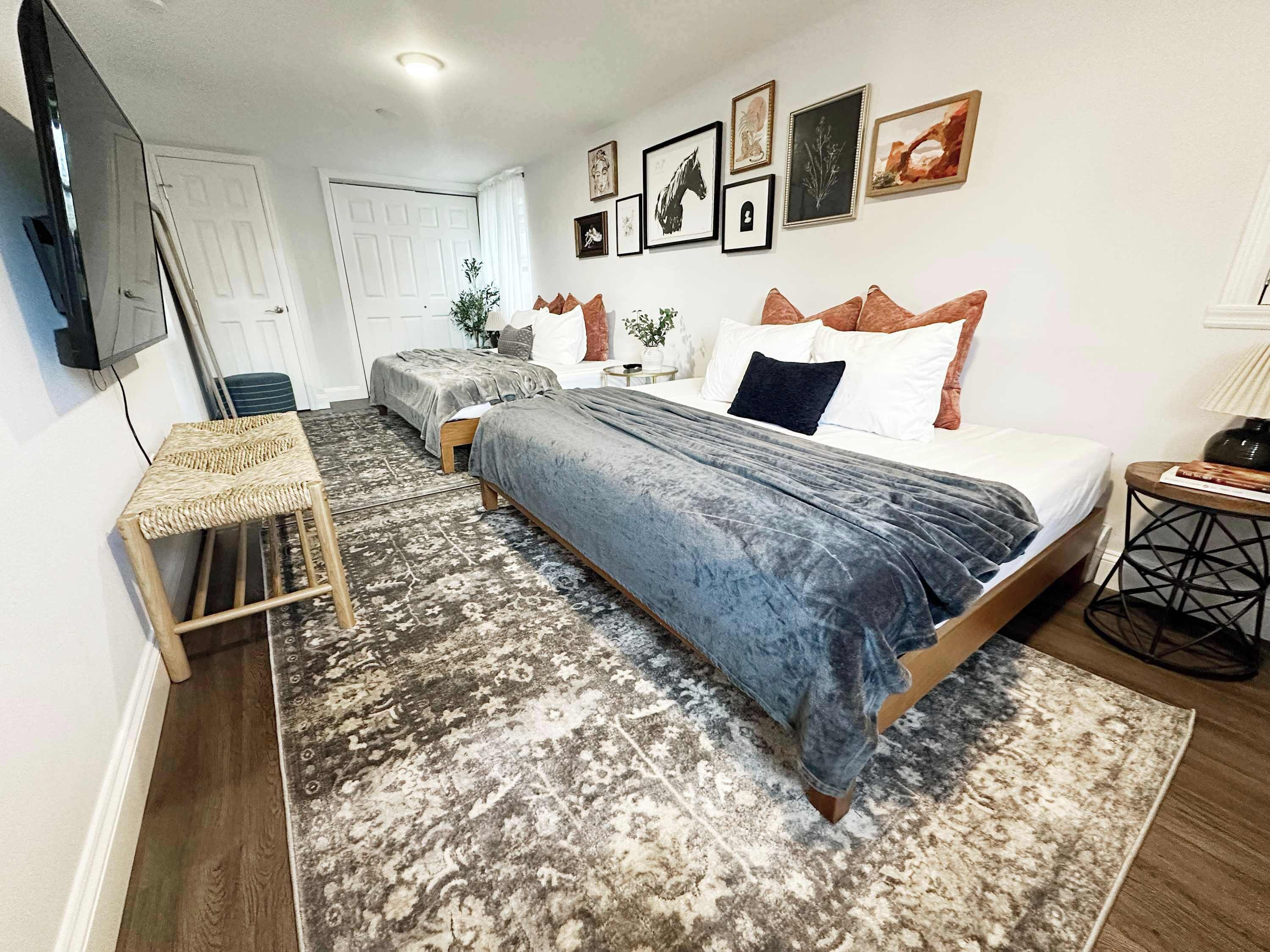 Un dormitorio con cama, mesitas de noche, televisor y televisor montado en la pared.