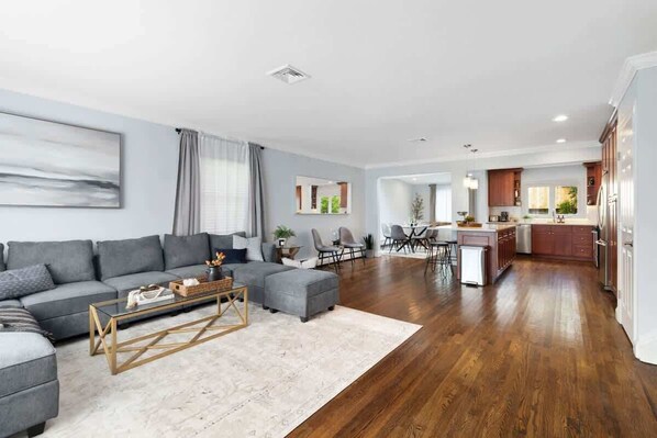 A modern living room with a grey sofa, a coffee table, and a dining area with chairs and a table.
