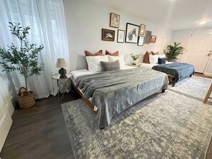 A bedroom with a bed, bedside tables, a lamp, a potted plant, and framed pictures on the wall.