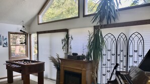 A cozy living room with a foosball table, a fireplace, a piano, and large windows.
