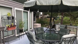 A deck with a glass-top table and chairs, surrounded by potted plants and a covered umbrella.