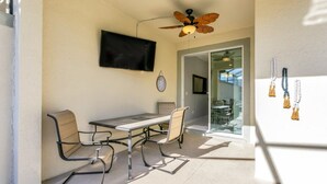 A sunlit patio with a table and chairs, a ceiling fan, and a TV mounted on the wall.