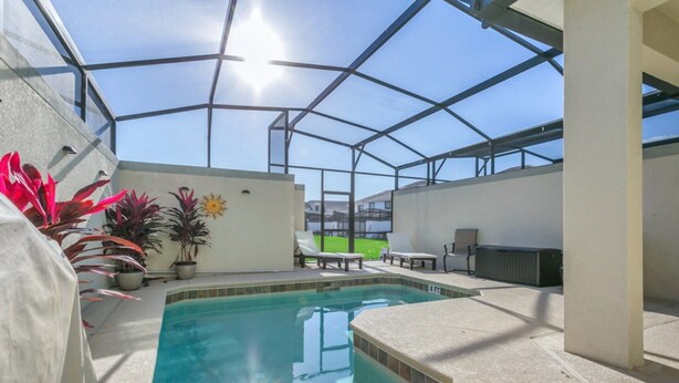 An indoor swimming pool with a glass ceiling, surrounded by lounge chairs and potted plants.