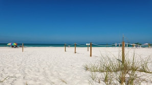 Une plage de sable blanc, un ciel bleu dégagé et quelques parasols.