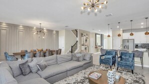 Een moderne woonkamer met een hoekbank, een salontafel en een eetgedeelte met een kroonluchter.