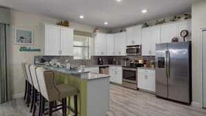 A modern kitchen with white cabinets, stainless steel appliances, and a bar area with stools. - The Ultimate 6 Bedroom Villa on Champions Gate Resort, Orlando Villa 4829 (Davenport)