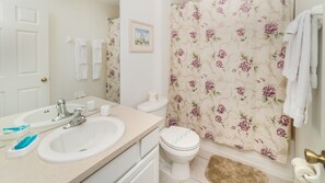 A bathroom with a sink, toilet, and shower curtain with a floral pattern. - Relax in Comfort at Villa 4947 (Kissimmee)