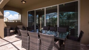 A patio area with wicker furniture and a glass table, overlooking a residential neighborhood.