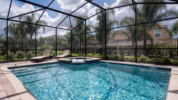 A swimming pool with a hot tub, surrounded by a glass enclosure and palm trees.