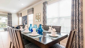 A dining area with a glass-top table, blue vases, and patterned curtains.
