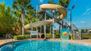 A pool with a slide, surrounded by palm trees and a clear sky. - Rent a Luxury Apartment on Windsor Hills Resort, Minutes From Disney, Orlando Apartment 3207 (Kissimmee)