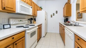 A kitchen with wooden cabinets, a white stove, a microwave, a refrigerator, and a dishwasher. - Rent a Luxury Apartment on Windsor Hills Resort, Minutes From Disney, Orlando Apartment 3207 (Kissimmee)