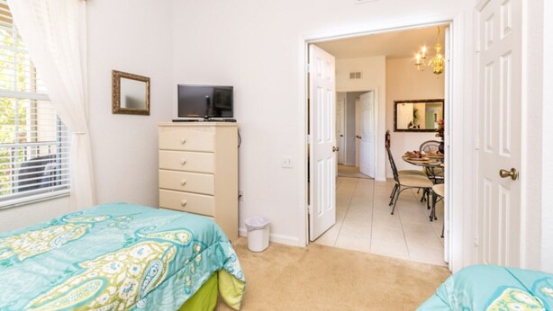 A bedroom with two beds, a dresser, a television, and a door leading to a dining area. - Rent a Luxury Apartment on Windsor Hills Resort, Minutes From Disney, Orlando Apartment 3207 (Kissimmee)