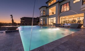 A modern pool area with a clear view of the pool, lounge chairs, and a multi-story building in the background. - Rent This Luxury 5 Star Villa on Reunion Resort and Spa, Orlando Mansion 4573 (Kissimmee)
