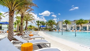 Un espace aménagé au bord de la piscine, avec des chaises longues, des palmiers et un ciel d’un bleu limpide.