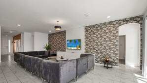 Un hall d’entrée moderne avec un mur en pierre, un grand canapé gris, un téléviseur et une plante en pot.